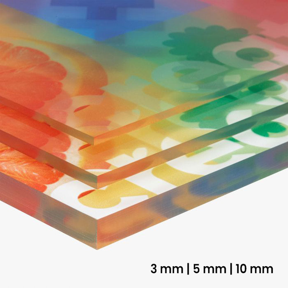 Nahaufnahme von mehreren übereinander gestapelten Acrylglasplatten. Sie sind transparent und rückseitig bedruckt mit grafischen Elementen und dem Wort "create". Die Platten sind in unterschiedlichen Stärken (3 mm, 5 mm, 10 mm) zu sehen. Am unteren Rand der Platten ist die scharfe Kante deutlich sichtbar.