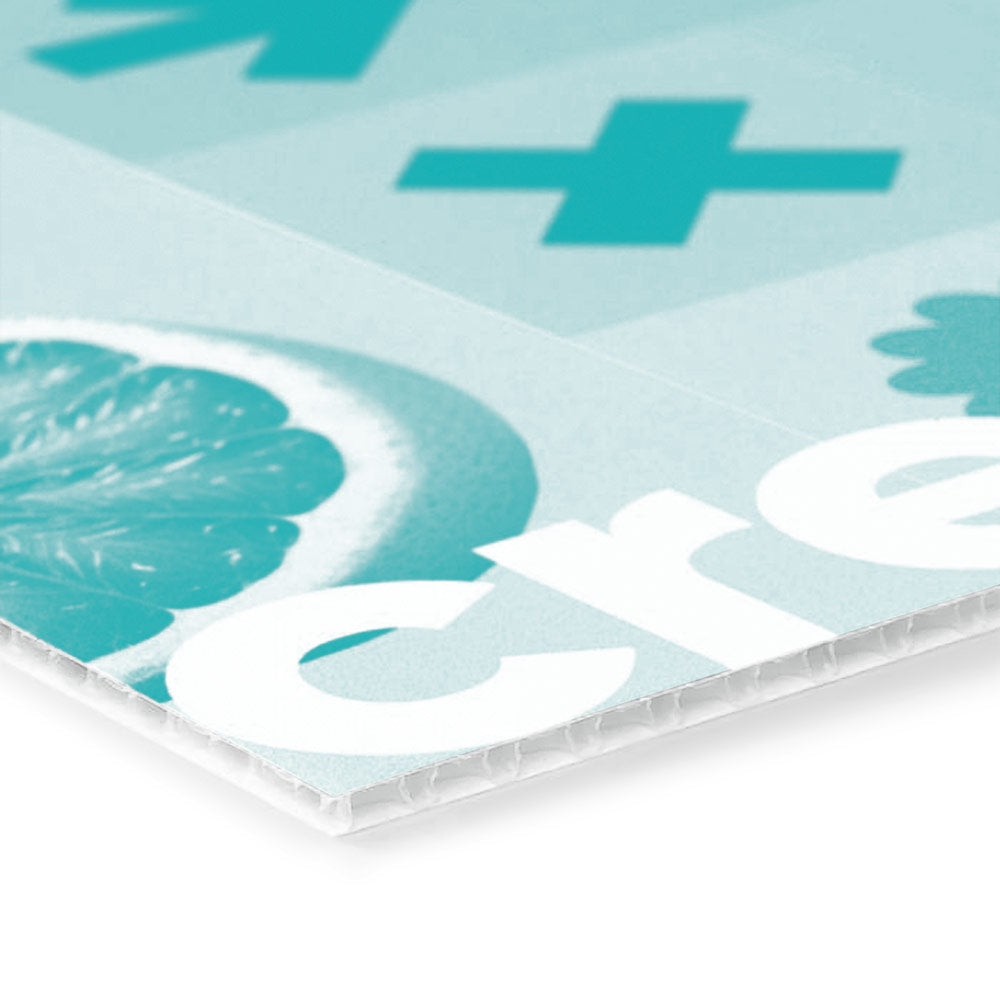 Das Bild zeigt einen Ausschnitt einer bedruckten Kunststoffplatte, auf der ein grafisches Design in sanften blauen Tönen zu sehen ist. Die Druckgrafik umfasst geometrische Symbole wie ein Pluszeichen sowie ein Stück Zitrusfrucht und den Schriftzug „create“. Die Kante der Platte ist deutlich sichtbar, was die Struktur des Materials zeigt.