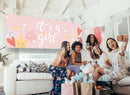 Rosa Babyshower-Banner mit "It's a Girl"-Schriftzug und süßen Illustrationen, dekorativ aufgehängt über einer fröhlichen Feier mit Freundinnen, die den besonderen Anlass genießen.