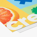 Dieses Bild zeigt einen detaillierten Ausschnitt eines bedruckten Materials, möglicherweise eines Banners oder Posters. Es ist zu erkennen, dass es sich um ein beschichtetes Material handelt, das mit einer fruchtigen Illustration (eine Grapefruit) und einem leuchtend gelben Hintergrund bedruckt ist. Die Textur des Druckmaterials ist gut sichtbar, mit einer fein strukturierten Oberfläche. Der Druck selbst scheint lebendige Farben zu verwenden.