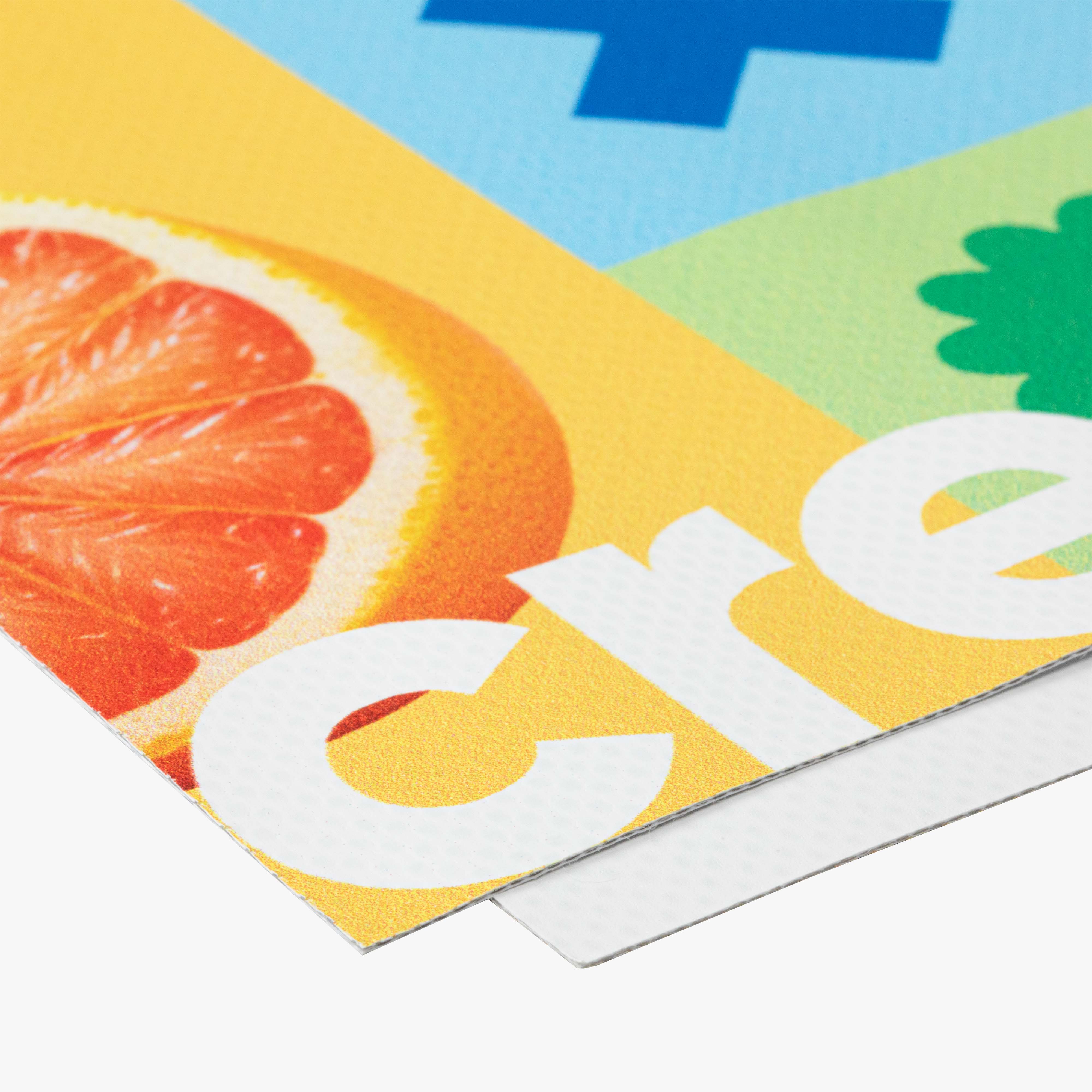 Dieses Bild zeigt einen detaillierten Ausschnitt eines bedruckten Materials, möglicherweise eines Banners oder Posters. Es ist zu erkennen, dass es sich um ein beschichtetes Material handelt, das mit einer fruchtigen Illustration (eine Grapefruit) und einem leuchtend gelben Hintergrund bedruckt ist. Die Textur des Druckmaterials ist gut sichtbar, mit einer fein strukturierten Oberfläche. Der Druck selbst scheint lebendige Farben zu verwenden.