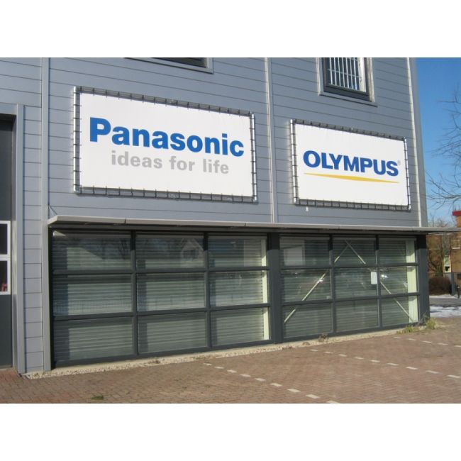 Zwei große Werbetafeln auf einem Gebäude. Die Tafeln zeigen die Logos von Panasonic mit dem Slogan "ideas for life" und von Olympus.
