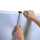 Detailaufnahme einer Hand, die eine Stange an einem Roll-up-Banner befestigt. Die Stange wird in eine Halterung eingeklinkt, um das Banner sicher zu fixieren. Die Oberfläche des Banners ist sichtbar, während die Person die Halterung anpasst. Der Hintergrund ist weiß, was die Konzentration auf die Handhabung des Banners ermöglicht.