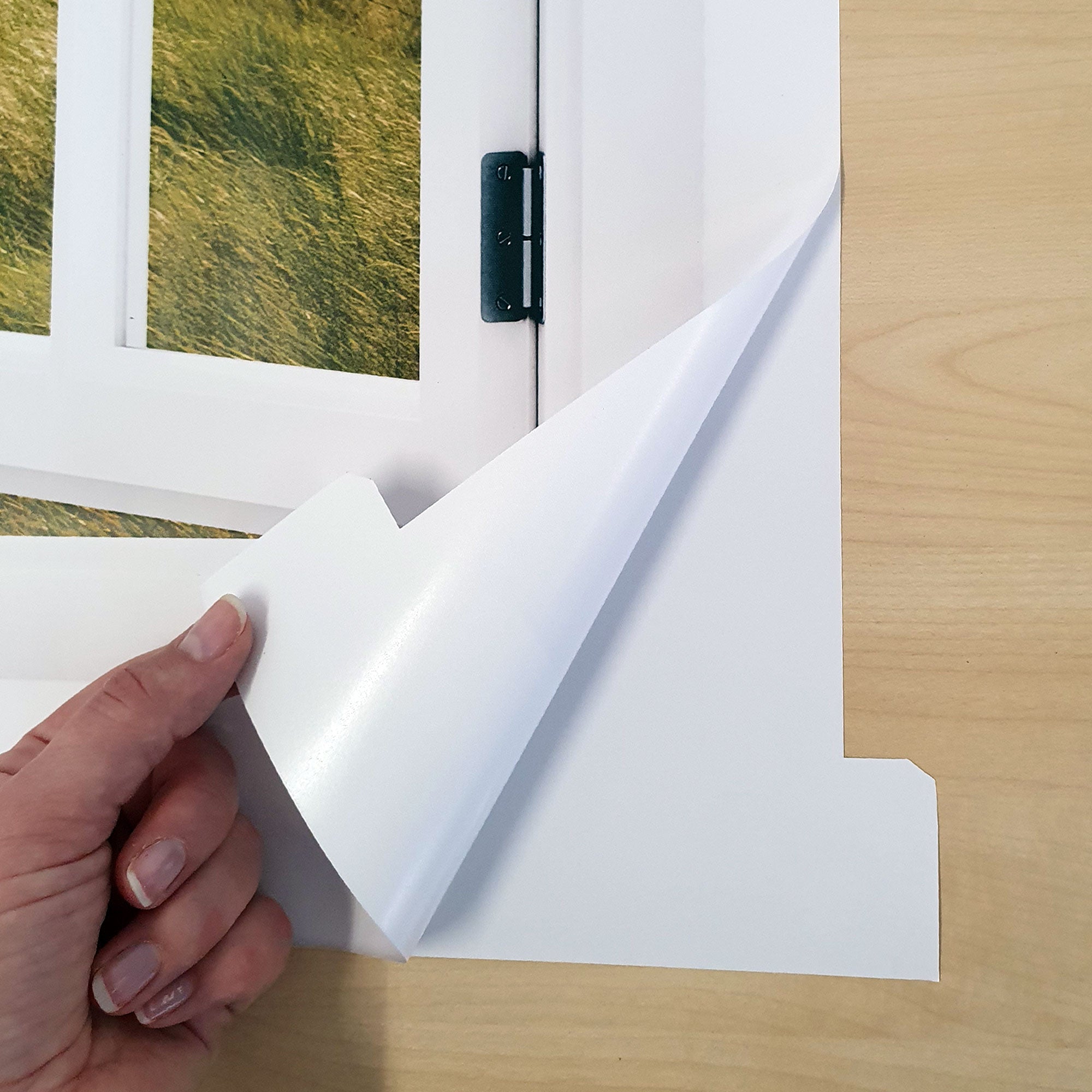 Detailansicht Wandaufkleber, Fensterblick, abgezogen mit der Hand an der rechten Ecke unten.