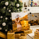 Stilvolles Leinwandbild mit einer Frau im Sonnenuntergang als besonderes Weihnachtsgeschenk, dekorativ unter einem geschmückten Weihnachtsbaum mit verpackten Geschenken arrangiert.