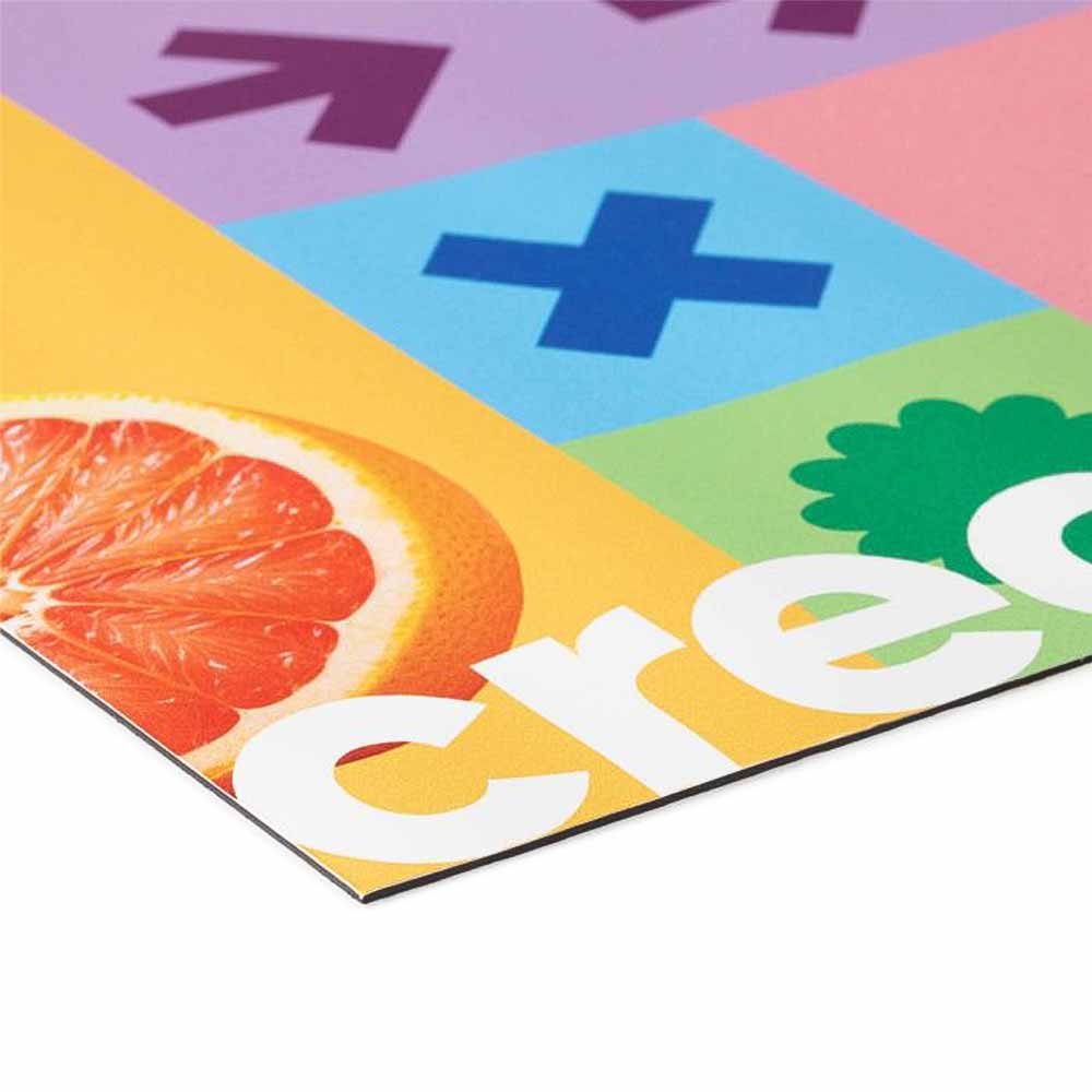 Nahaufnahme eines bunten Plakats, das eine orangefarbene Grapefruit und das Wort "crea" in weißen Buchstaben zeigt. Der Hintergrund ist in verschiedenen bunten Feldern (rosa, blau, gelb, grün) mit Symbolen wie Pfeilen und Pluszeichen unterteilt.