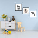 Drei Illustrationen von einem Koi-Fisch, Tintenfisch und Delfin in schwarz-weißer Farbgebung, eingerahmt und an einer Wand im Kinderzimmer angebracht, umgeben von Spielzeug und einer Kinderstuhleinrichtung.