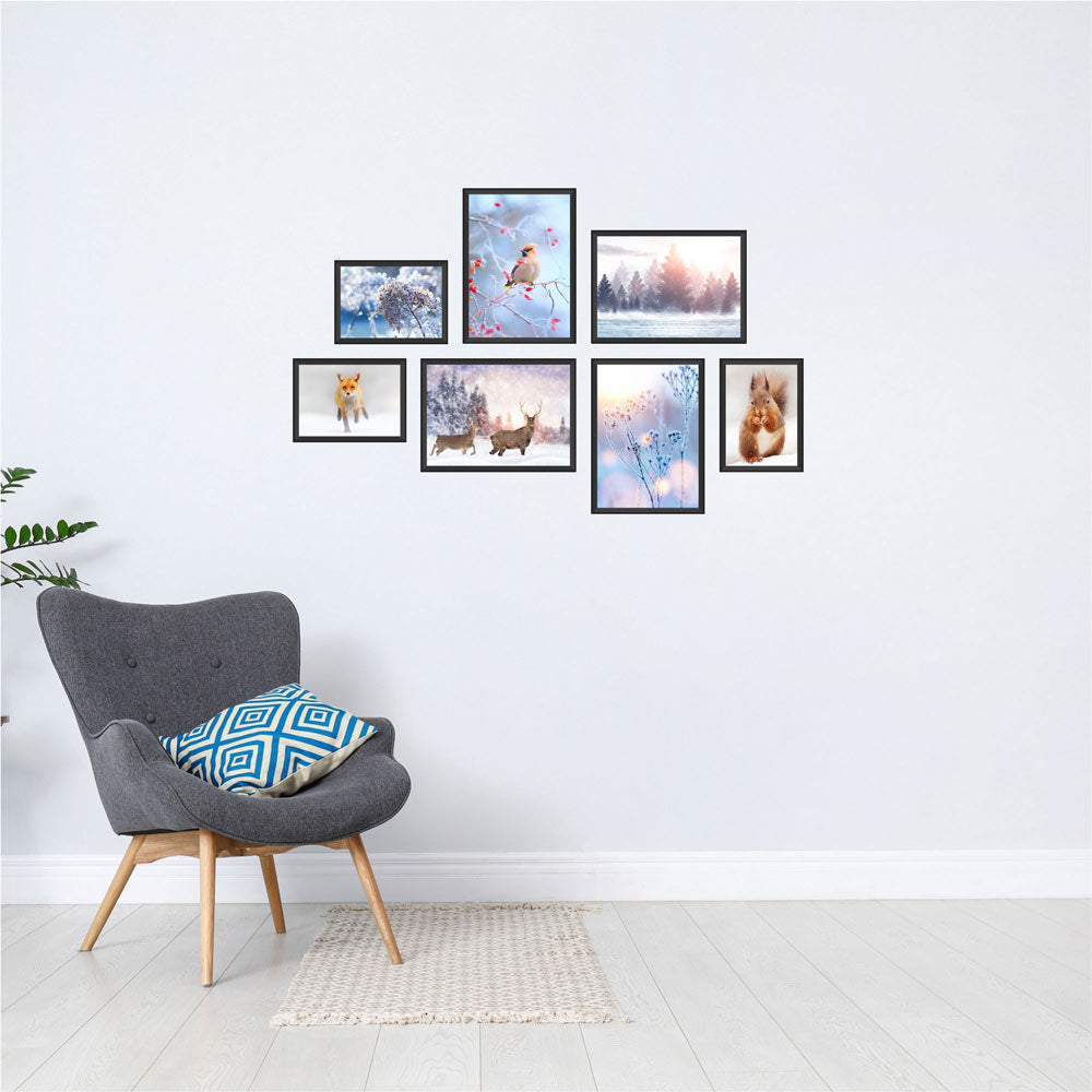 Poster-Collage mit winterlichen Naturmotiven: Vögel, Rehe, Fuchs, Eichhörnchen und verschneite Landschaften – stimmungsvolle Wanddeko im Winter-Design. Das sind die Vorderansichten von dem Winter-Set, als Dekoidee in schwarzen Rahmen an einer weissen Wand neben einem grauen Sessel.