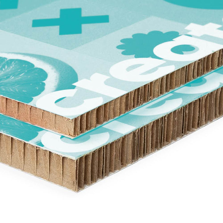 Nahaufnahme von zwei übereinander liegenden, bedruckten Pappplatten, die eine türkisfarbene Grafik mit Zitronenmotiv und dem Text "create" zeigen. Die Kanten der Platten sind wellenförmig und bestehen aus braunem Wellpappe-Material.