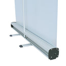 Ein Roll-Up-Banner in einer aufgestellten Position. Der Mechanismus und die Basis des Ständers sind gut sichtbar. Das Banner ist aufgerollt und wird von einem weißen Stützrohr gehalten, das auf einem stabilen Aluminiumgehäuse mit abgerundeten Ecken ruht. Der Ständer ist aus silbernem Aluminium gefertigt und bietet eine solide Unterstützung für das Display.