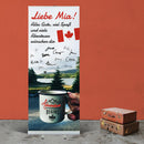 Ein Roll-up-Banner für Mia mit einer persönlichen Nachricht ihrer Freunde und Familie. Es zeigt den Text „Liebe Mia! Alles Gute, viel Spaß und viele Abenteuer wünschen dir“ zusammen mit einer handgeschriebenen Unterschrift von mehreren Personen. Das Banner enthält ein Bild von einem Becher mit dem Schriftzug „The Adventure Begins“, während im Hintergrund eine malerische Aussicht auf einen See und Bäume zu sehen ist. Es sind auch zwei kanadische Flaggen abgebildet.