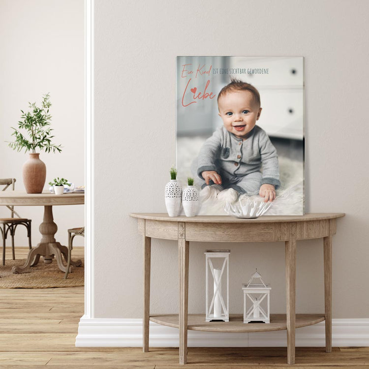 Acrylglasbild mit Babyfoto und Zitat „Ein Kind ist eine sichtbar gewordene Liebe“, dekorativ auf einem Tisch im Wohnzimmer platziert.
