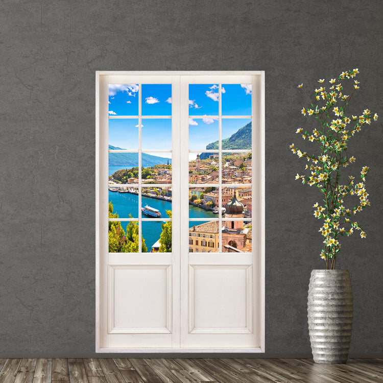 Hingucker für dunkle Räume oder ohne Fenster, selbstklebendes Wandtattoo als Terrassentür mit dem Blick Dorf am See im Sommer. Hier an einer dunklen Wand verklebt neben einer Bodenvase.