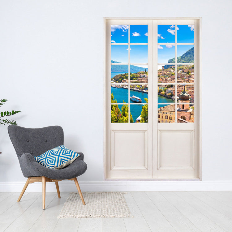 Gedrucktes Wandbild für Tapete und Möbel, mit toller Aussicht auf türkisfarbenen See und einem Dorf. Der Terrassentür Aufkleber ist an einer weissen Wand neben einem grauen Sessel verklebt.