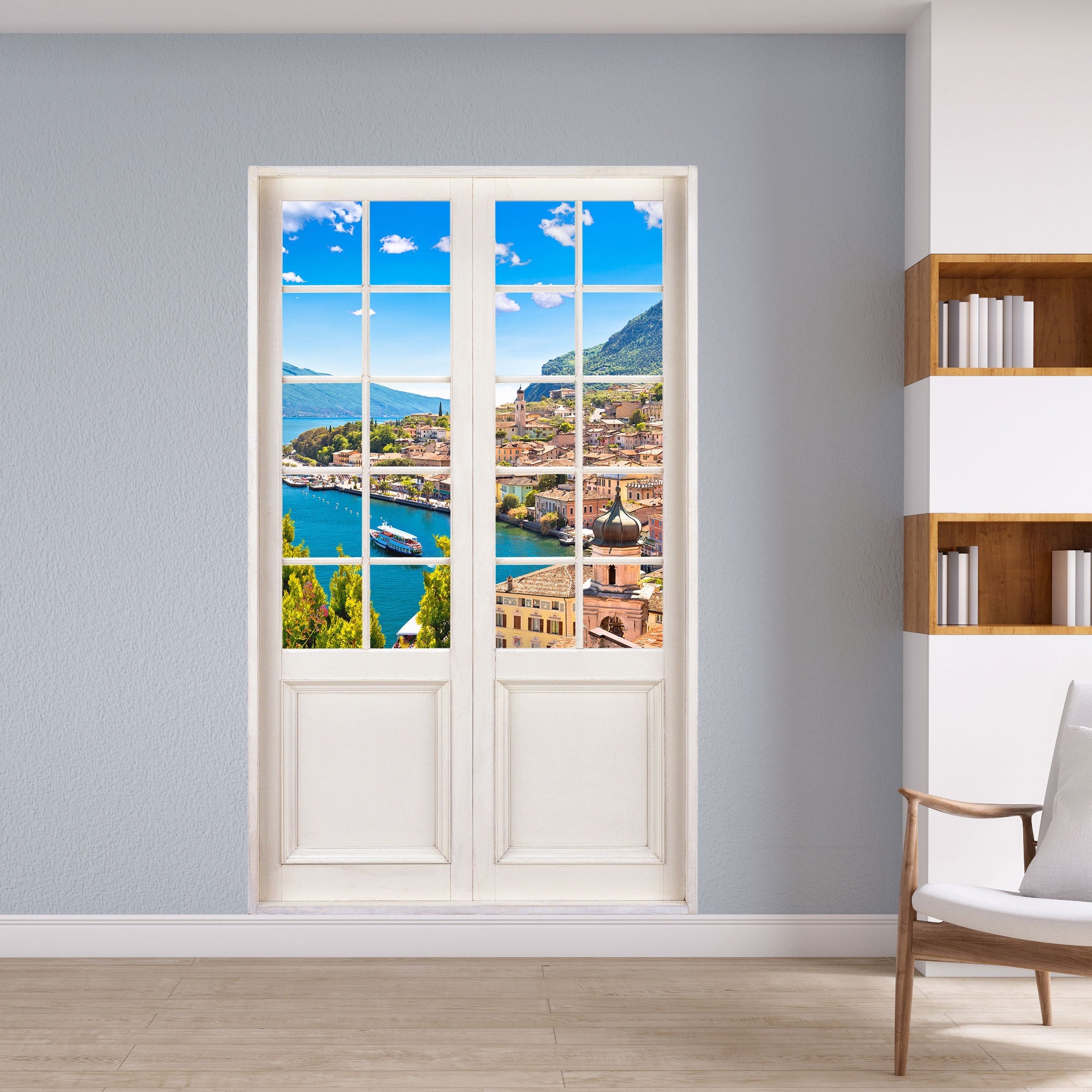 Wandaufkleber für Wohn- und Schlafzimmer, vergrößert Ihr Zimmer optisch und bringt Urlaubsfeeling. Hier das Motiv Dorf am See im Sommer hinter weisser Terrassentür an einer grauen Wand, neben einem Regal.