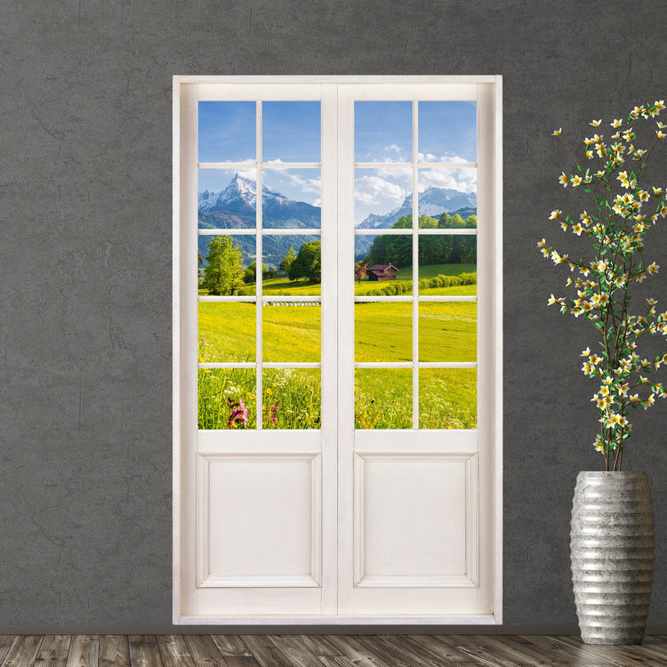 Selbstklebende Tapete mit Terrassentür für Ausblick auf idyllische Natur, Motiv: Alpenblick mit grüner Wiese. Als Dekoidee an einer grauen Wand verklebt, neben einer Bodenvase. 