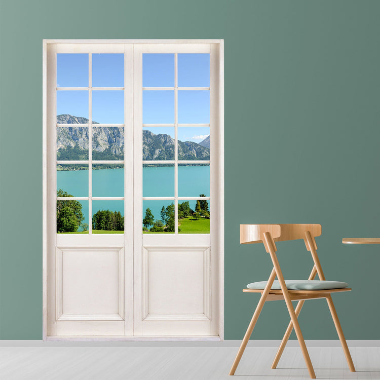 Moderner Essbereich mit Blickfang für Ihre Wohndekoration. Flügeltür mit optischer Täuschung und Ausblick auf einen wunderschönen See und Berge. Der Wandaufkleber ist als Idee an einer grünen Wand in einem Essbereich verklebt.