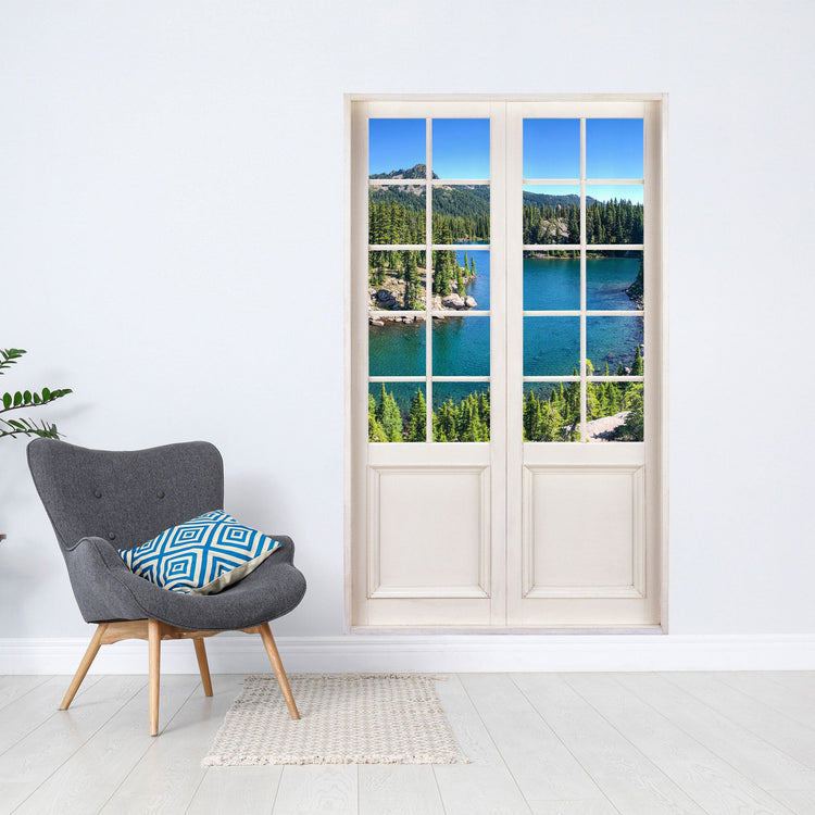 Wandtattoo bedruckt mit dem Bild einer weissen Sprossen-Terrassentür und Blick auf einen Bergsee mit Bergen und Wald. Als Größenvorstellung neben einem Sessel an der Wand verklebt.