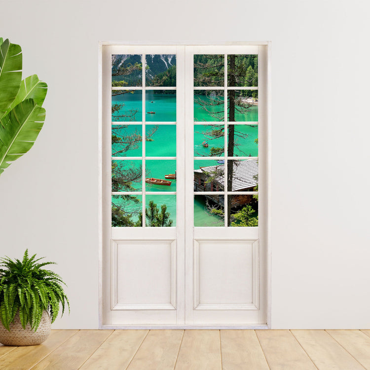 Hingucker für dunkle Räume oder ohne Fenster. Selbstklebendes Wandtattoo als Terrassentür mit dem Blick auf einen Bergsee. Hier als Beispiel an einer weissen Wand neben Zimmerpflanzen verklebt.