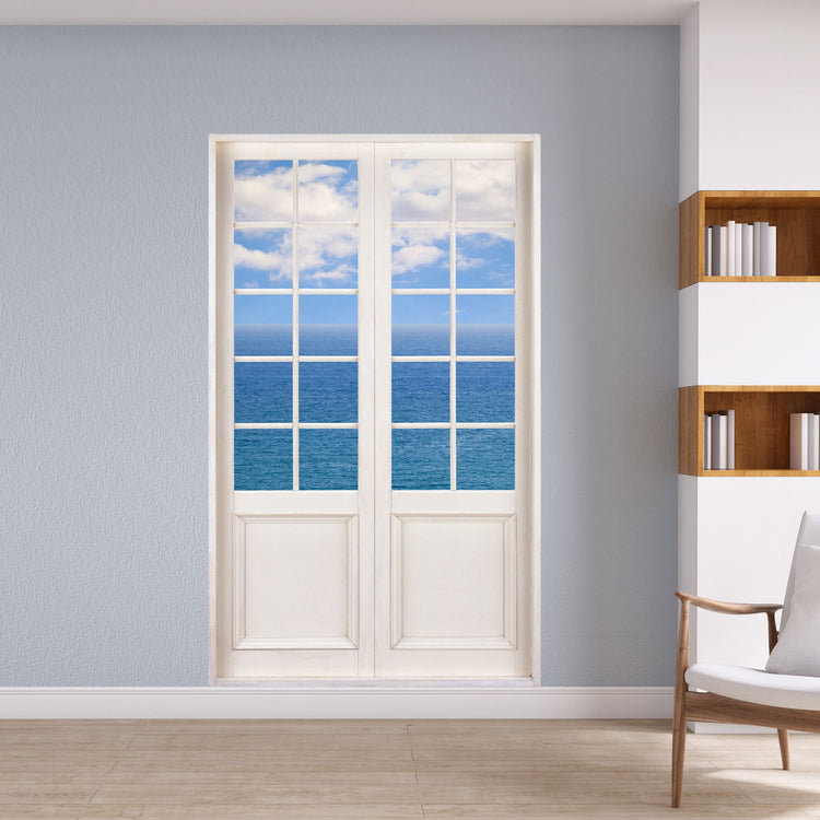 Wandtattoo 120x200cm bedruckt mit dem Bild deiner Terrassentür und Blick auf den Ozean mit blauem Himmel und weissen Wolken für einen 3D Effekt. Hier an einer grauen Wand verklebt, neben einem Sessel und einem Bücherregal.