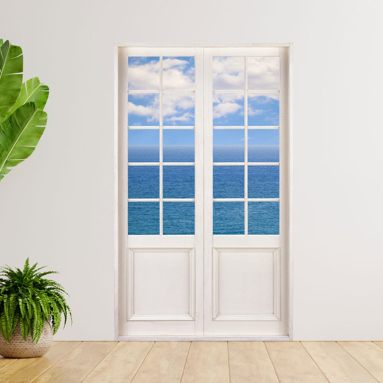 Hingucker für dunkle Räume oder ohne Fenster, selbstklebendes Wandtattoo als Terrassentür mit dem Foto auf das Meer und blauem Himmel. An einer weissen Wand neben großen Zimmerpflanzen.