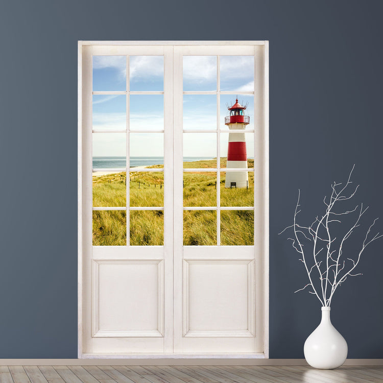 Wandtattoo Klebetapete mit Motiv einer Glastür und Ausblick in die Natur. Motiv Ostsee, Dünen und einem Leuchtturm in der Größe 120x200cm, an einer blauen Wand neben einer Bodenvase.