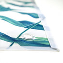 Das Bild zeigt einen näheren Blick auf die Ecke eines bedruckten Materials, möglicherweise ein Banner oder eine Werbeplane. Der Stoff zeigt grüne Blätter und die Naht an der Kante ist gut sichtbar. An der Ecke befindet sich ein Ösenloch, das wahrscheinlich zum Aufhängen oder Befestigen des Banners verwendet wird. Die Verwendung von Metallösen ist typisch für Werbebanner oder Planen, die an öffentlichen Orten aufgehängt werden.
