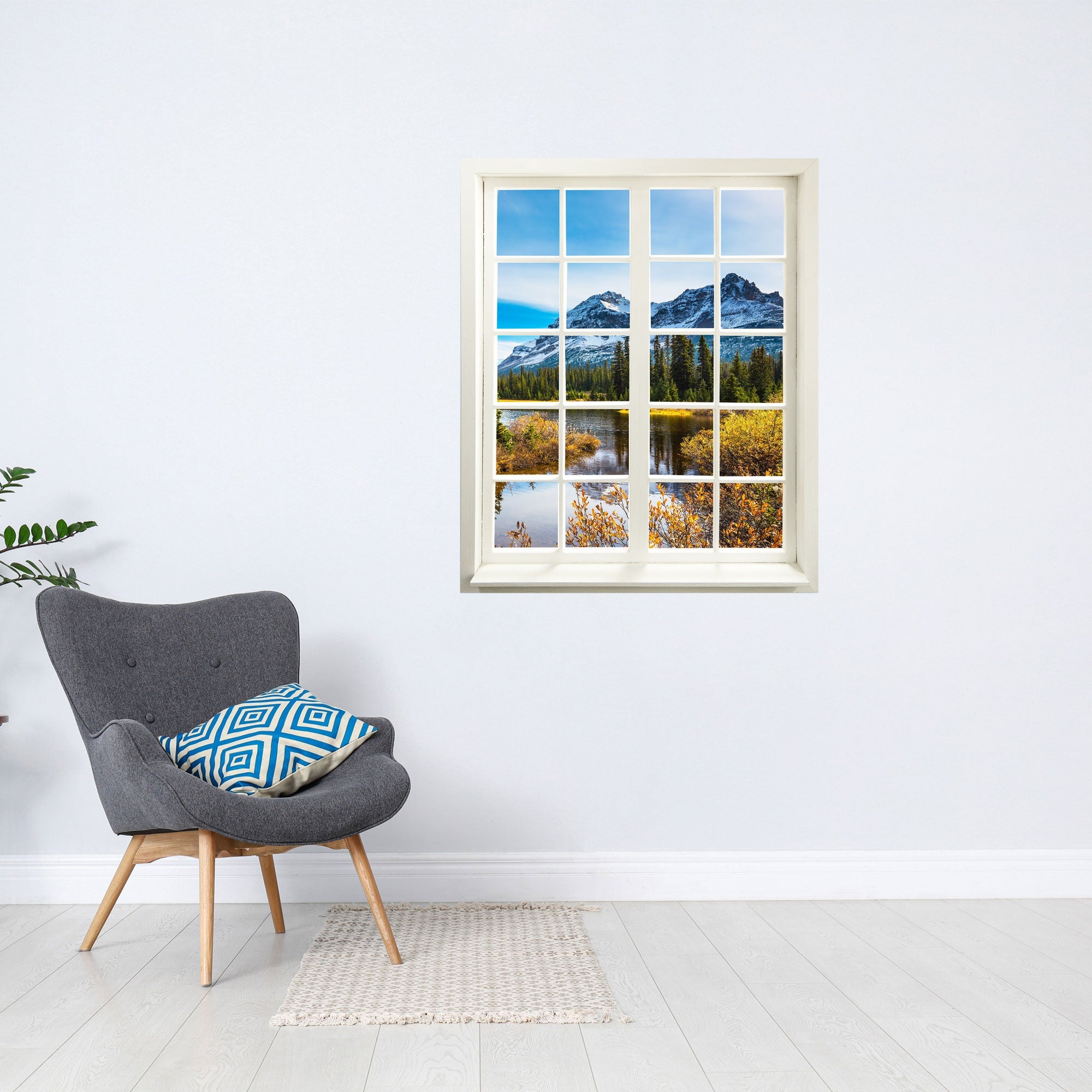 Wandaufkleber Sprossenfenster mit toller Aussicht auf ein Bergmassiv mit Fluss, vergrößert Zimmer optisch. An einer weissen Wand über einem grauen Sessel, mit Kissen und Teppich.