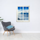 Selbstklebende Wandaufkleber - Fensterblick geschlossen Motiv "Berge und See". An einer weissen Wand über einem grauen Sessel.