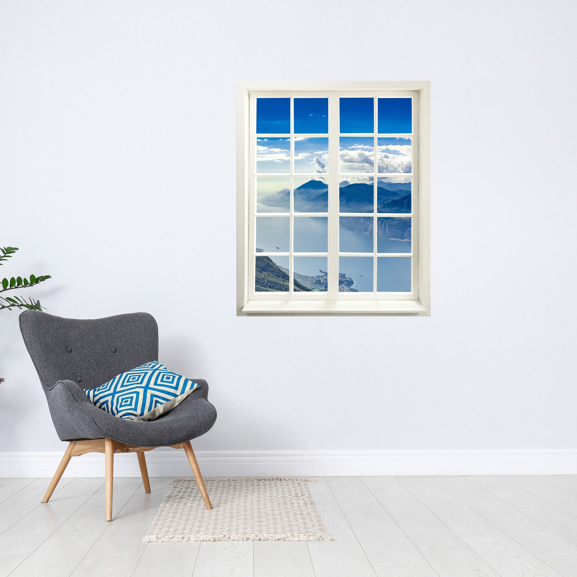 Selbstklebende Wandaufkleber - Fensterblick geschlossen Motiv "Berge und See". An einer weissen Wand über einem grauen Sessel.