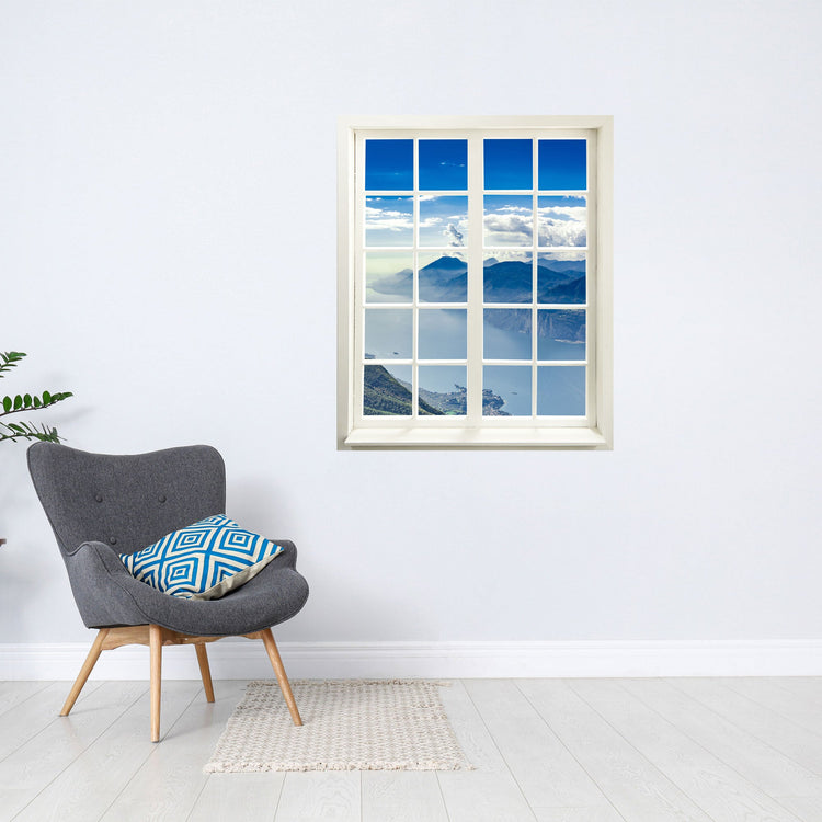 Selbstklebende Wandaufkleber - Fensterblick geschlossen Motiv "Berge und See". An einer weissen Wand über einem grauen Sessel.