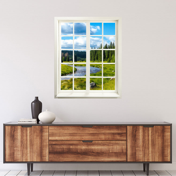 Wandtattoo Sprossenfenster Aufkleber mit Aussicht in die Natur, blauer Himmel mit grüner Wiese und Tannenwald. Motiv "Fluss-Landschaft" über einer braunen Kommode.