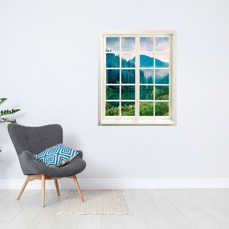 Wandtattoo bedruckt mit Fensterrahmen und tollem Naturbild vom "Tannenwald mit See" über einem grauen Sessel an der Wand.
