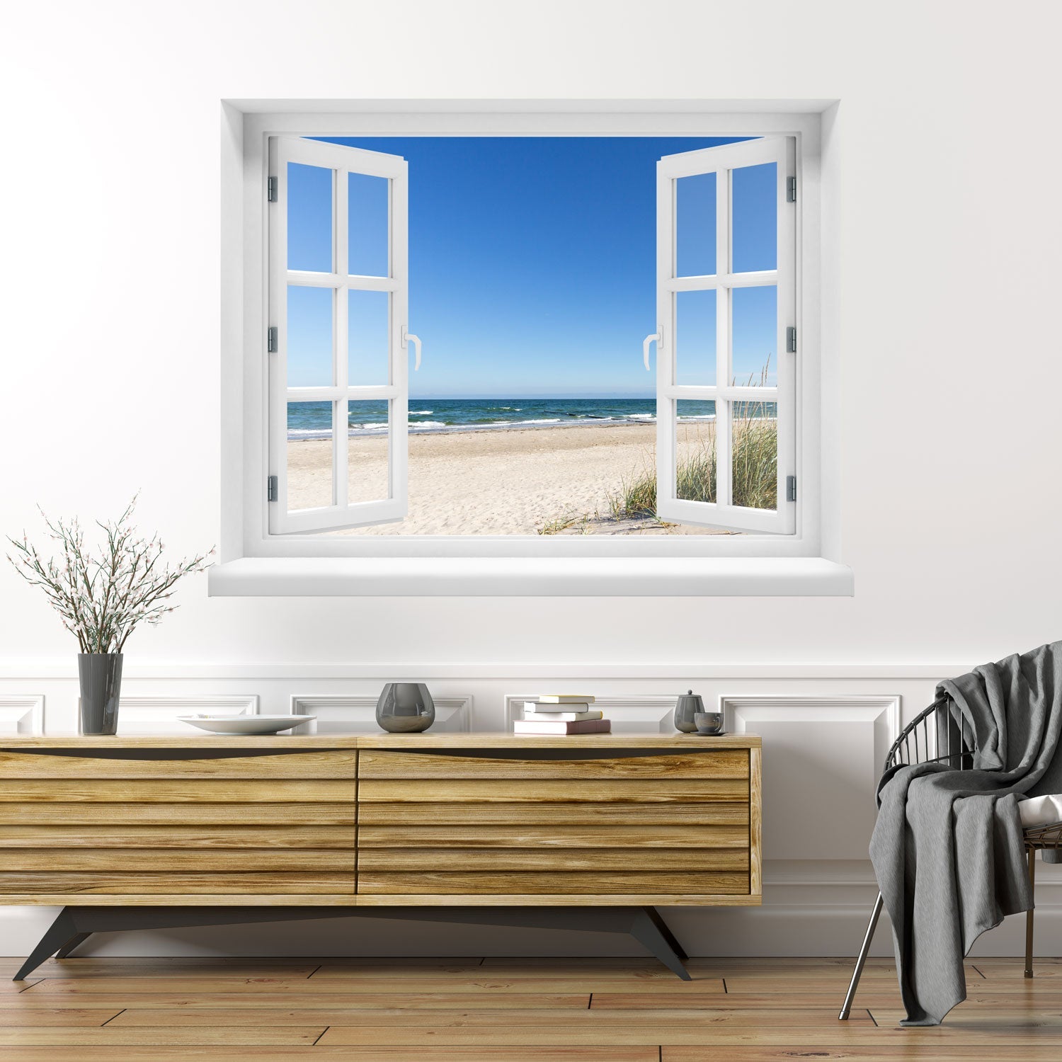 Offenes Fenster mit Blick auf Sandstrand, Meer und blauen Himmel – dekorativer Wandaufkleber mit 3D-Effekt für sommerliches Urlaubsfeeling im eigenen Zuhause. Als Dekoidee an einer weissen Wand über einer Holz Kommode verklebt.