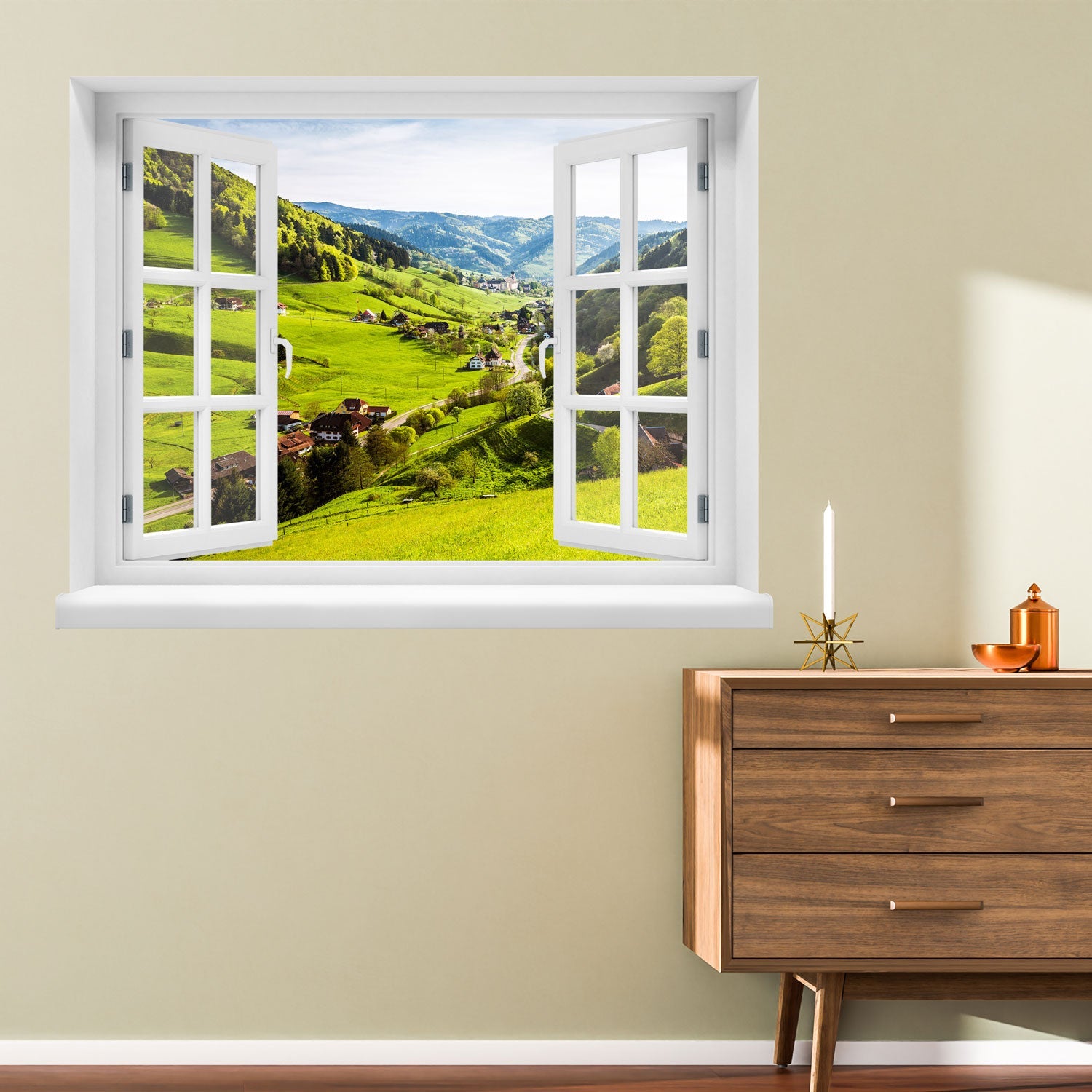 Offenes Fenster mit Ausblick auf grüne Hügel, ein idyllisches Dorf und bewaldete Berge – dekoratives Fensterbild mit realistischer 3D-Optik für naturnahes Wohnambiente. Als Dekoidee an einer gelben Wand neben einer Kommode aus Holz verklebt.