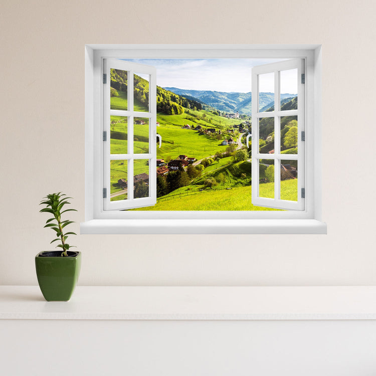 Offenes Fenster mit Ausblick auf grüne Hügel, ein idyllisches Dorf und bewaldete Berge – dekoratives Fensterbild mit realistischer 3D-Optik für naturnahes Wohnambiente. Als Dekoidee an einer beigen Wand neben einer Zimmerpflanze verklebt.