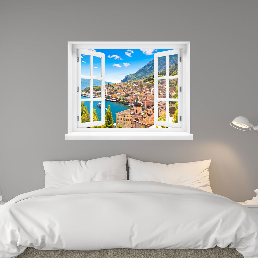 Wandaufkleber mit dem Fensterblick "Dorf am See" an einer grauen Wand über dem Bett verklebt.