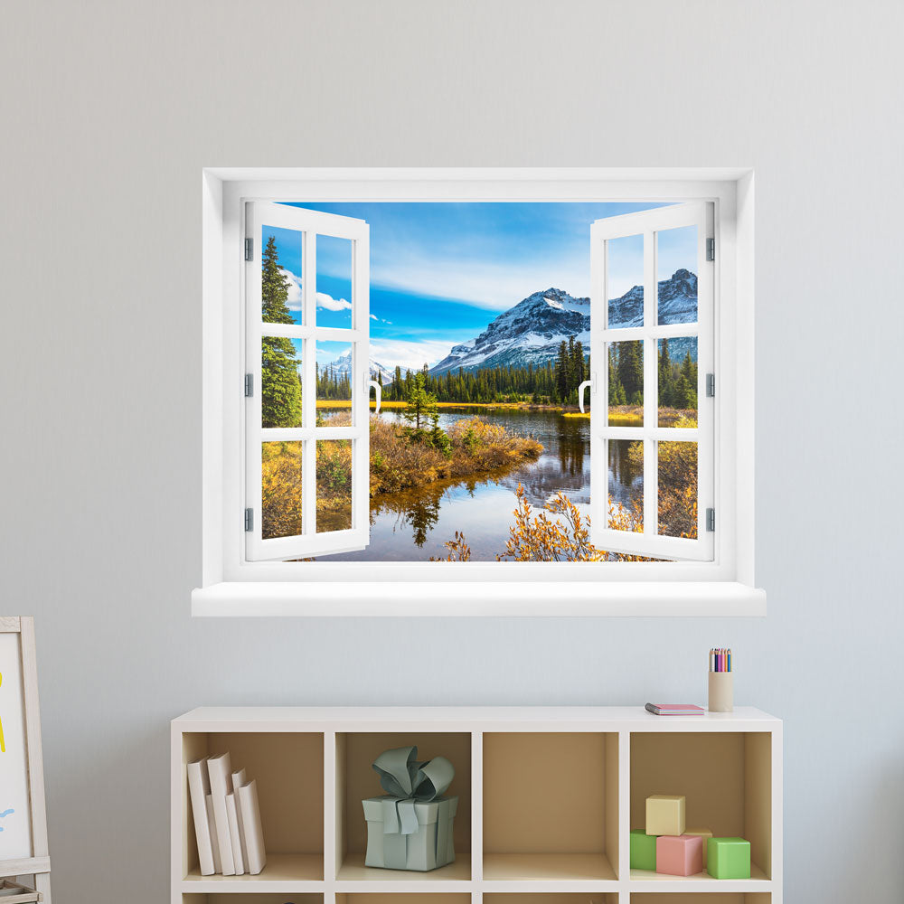 Wandaufkleber-Ansicht: offenes Fenster mit Blick auf eine idyllische Berglandschaft mit schneebedeckten Gipfeln, Nadelbäumen und einem ruhigen See im Vordergrund – Naturpanorama im Herbst. Als Dekoidee verklebt an einer weissen Wand im Kinderzimmer über einem Regal.