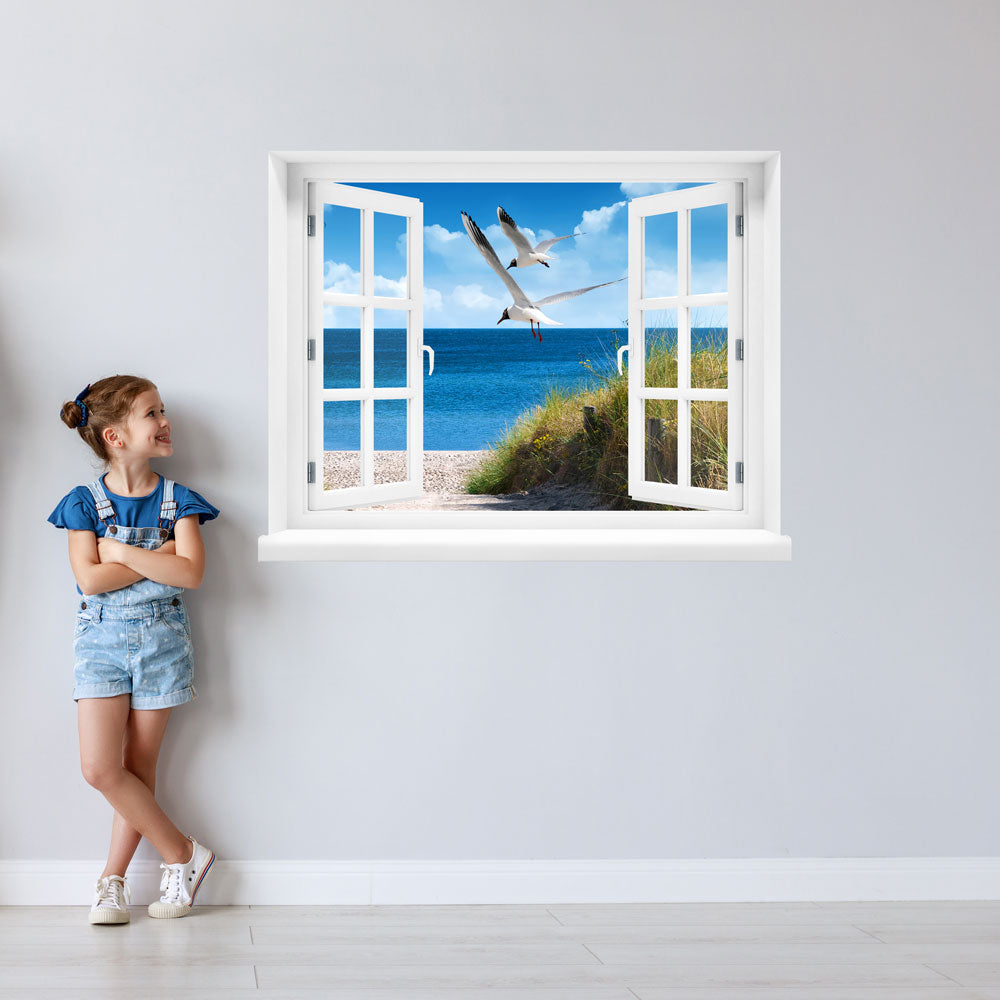 Wandtattoo bedruckt mit Fensterrahmen und tollem Naturbild Ostsee "Strand mit Möwen" an einer Wand neben einem Mädchen, das zum Aufkleber guckt.