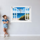 Wandtattoo bedruckt mit Fensterrahmen und tollem Naturbild Ostsee "Strand mit Möwen" an einer Wand neben einem Mädchen, das zum Aufkleber guckt.