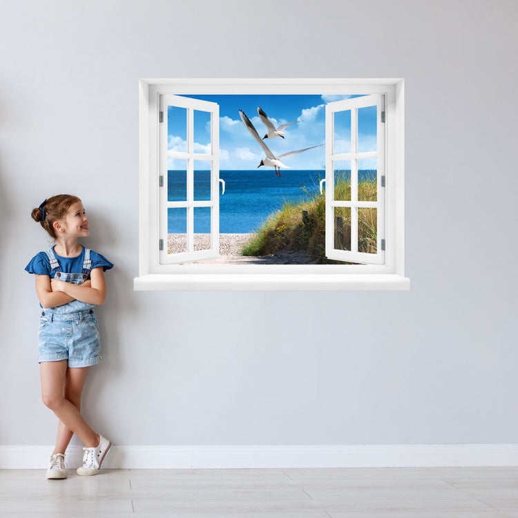 Wandtattoo bedruckt mit Fensterrahmen und tollem Naturbild Ostsee "Strand mit Möwen" an einer Wand neben einem Mädchen, das zum Aufkleber guckt.