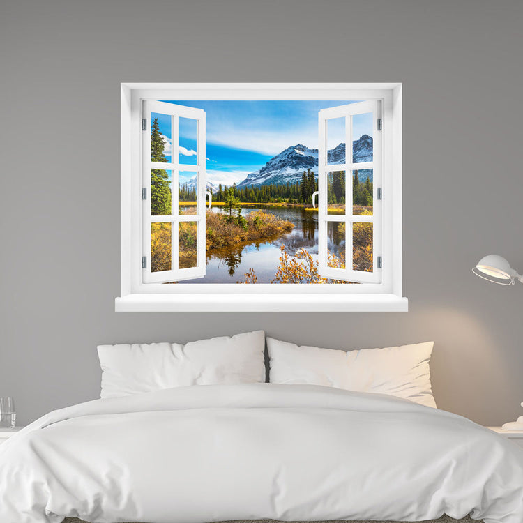 Wandaufkleber-Ansicht: offenes Fenster mit Blick auf eine idyllische Berglandschaft mit schneebedeckten Gipfeln, Nadelbäumen und einem ruhigen See im Vordergrund – Naturpanorama im Herbst. Als Dekoidee verklebt an einer grauen Wand über dem Bett im Schlafzimmer.