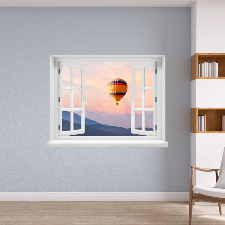 Wandaufkleber mit dem Motiv offenes Fenster mit Blick auf einen Heißluftballon im Sonnenuntergang über einer Berglandschaft – dekoratives 3D-Fensterbild mit Panorama-Effekt. Als Dekoidee an einer hellblauen Wand in einer Lesecke.