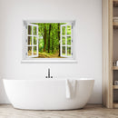 Wandaufkleber Ansicht eines offenes Fenster mit Blick in einen sonnendurchfluteten, grünen Laubwald mit einem schmalen Waldweg – entspannende Naturkulisse mit Frühlings- oder Sommerstimmung. Als Dekoidee in einem Badezimmer, über einer modernen Badewanne an der weissen Wand verklebt.