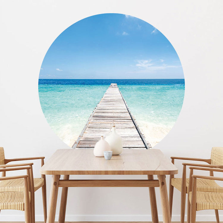 Großansicht eines runden Wandaufklebers mit einem Motiv vom Steg in der Karibik mit blauem Meer. Das Bild schafft einen 3D Effekt und sorgt für eine Tiefe. Als Dekoidee ist es an einer weissen Wand verklebt über einem Esstisch aus Holz.