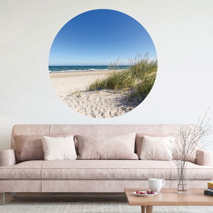 Großansicht eines runden Wandaufklebers mit einem Motiv von Ostseedünen, Strand und dem Meer. Das Bild schafft einen 3D Effekt und sorgt für eine Tiefe. Als Dekoidee ist das Wandtattoo an einer weissen Wand verklebt über einer beigen Couch.