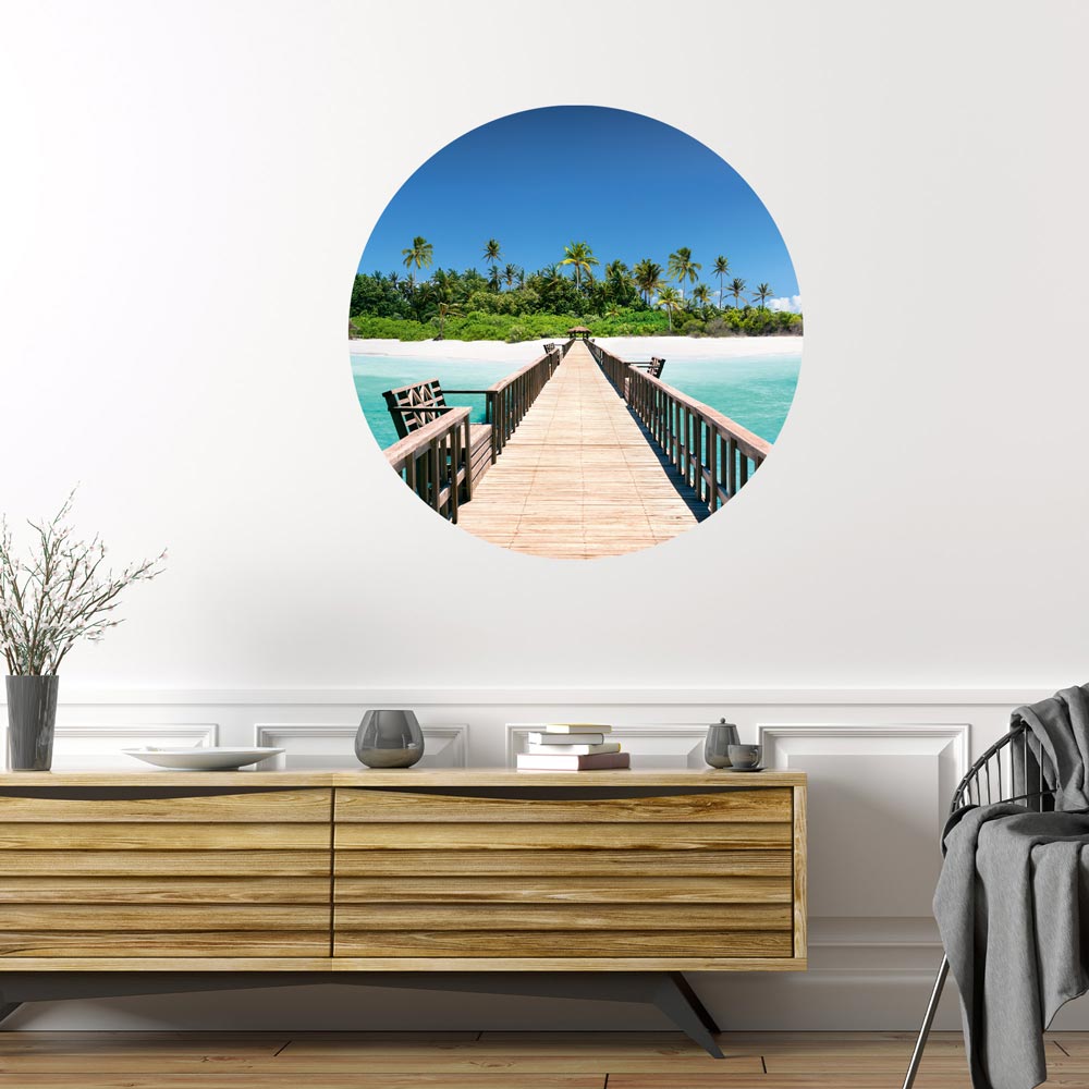Großansicht eines runden Wandaufklebers mit einem Motiv von Palmen in einer Lagune. Das Bild schafft einen 3D Effekt und sorgt für eine Tiefe. Als Dekoidee ist das Wandtattoo an einer weissen Wand verklebt über einer Holz-Kommode.