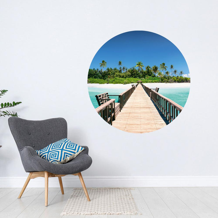 Großansicht eines runden Wandaufklebers mit einem Motiv von Palmen in einer Lagune. Das Bild schafft einen 3D Effekt und sorgt für eine Tiefe. Als Dekoidee ist das Wandtattoo an einer weissen Wand verklebt über einem grauen Sessel.