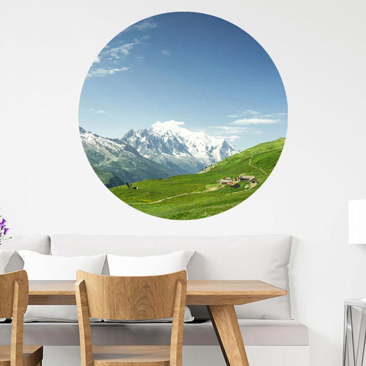 Ein großer, runder, Wandaufkleber mit einem Alpen-Wiesen-Motiv ist an einer Wand verklebt. Es ist eine Dekoidee über einer Couch mit Essbereich und für verschieden Räume möglich, die einen 3D Effekt schaffen.