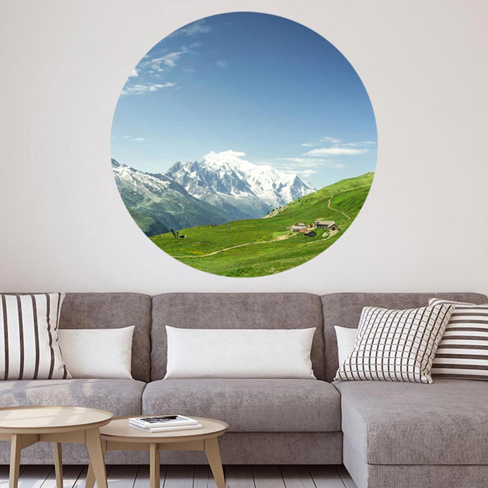 Ein großer, runder, Wandaufkleber mit einem Alpen-Wiesen-Motiv ist an einer Wand verklebt. Es ist eine Dekoidee über einer Wohn-Couch und für verschieden Räume möglich, die einen 3D Effekt schaffen.